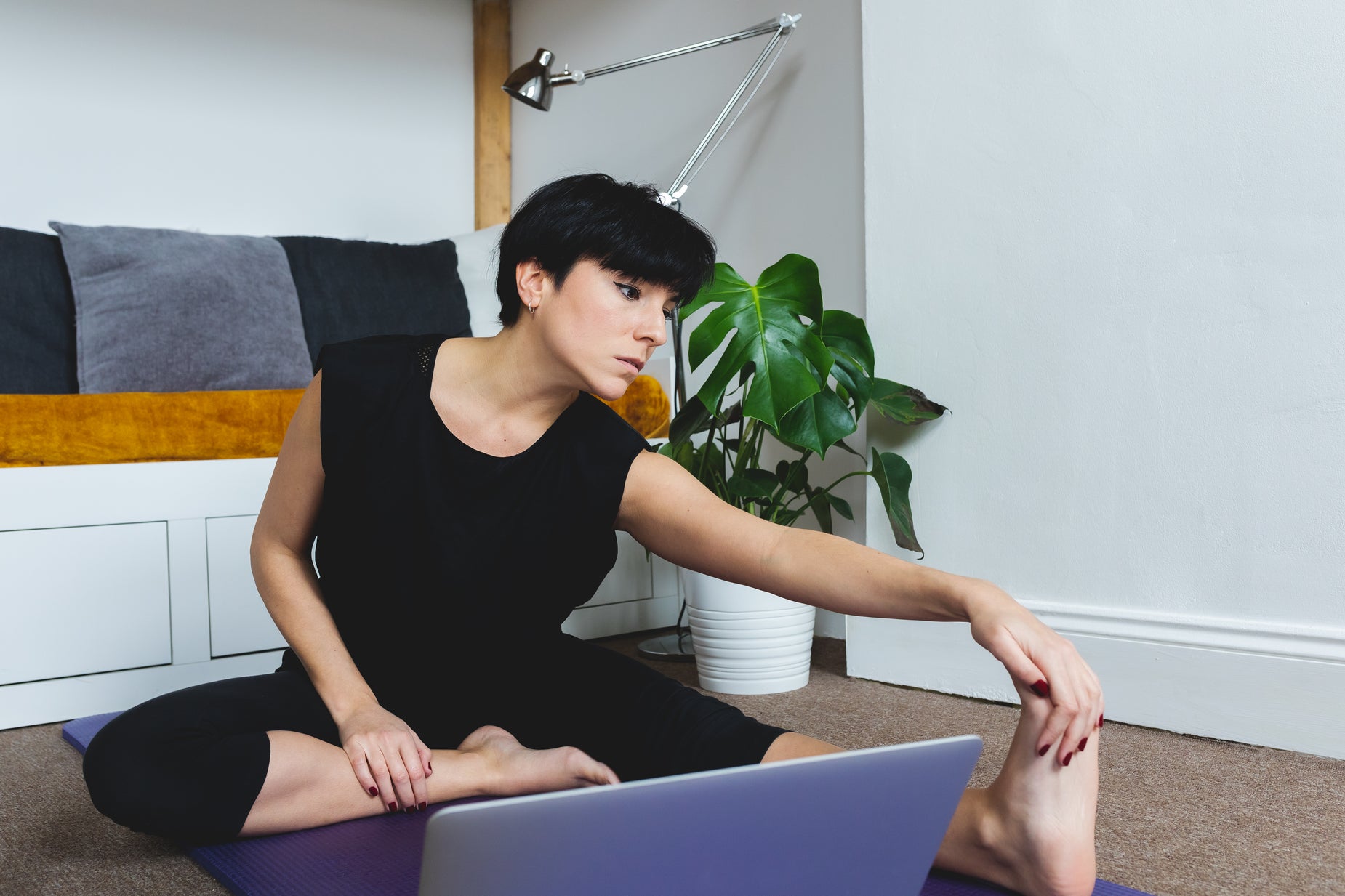 "Woman sitting on a yoga mat stretching her outstretched leg at home"